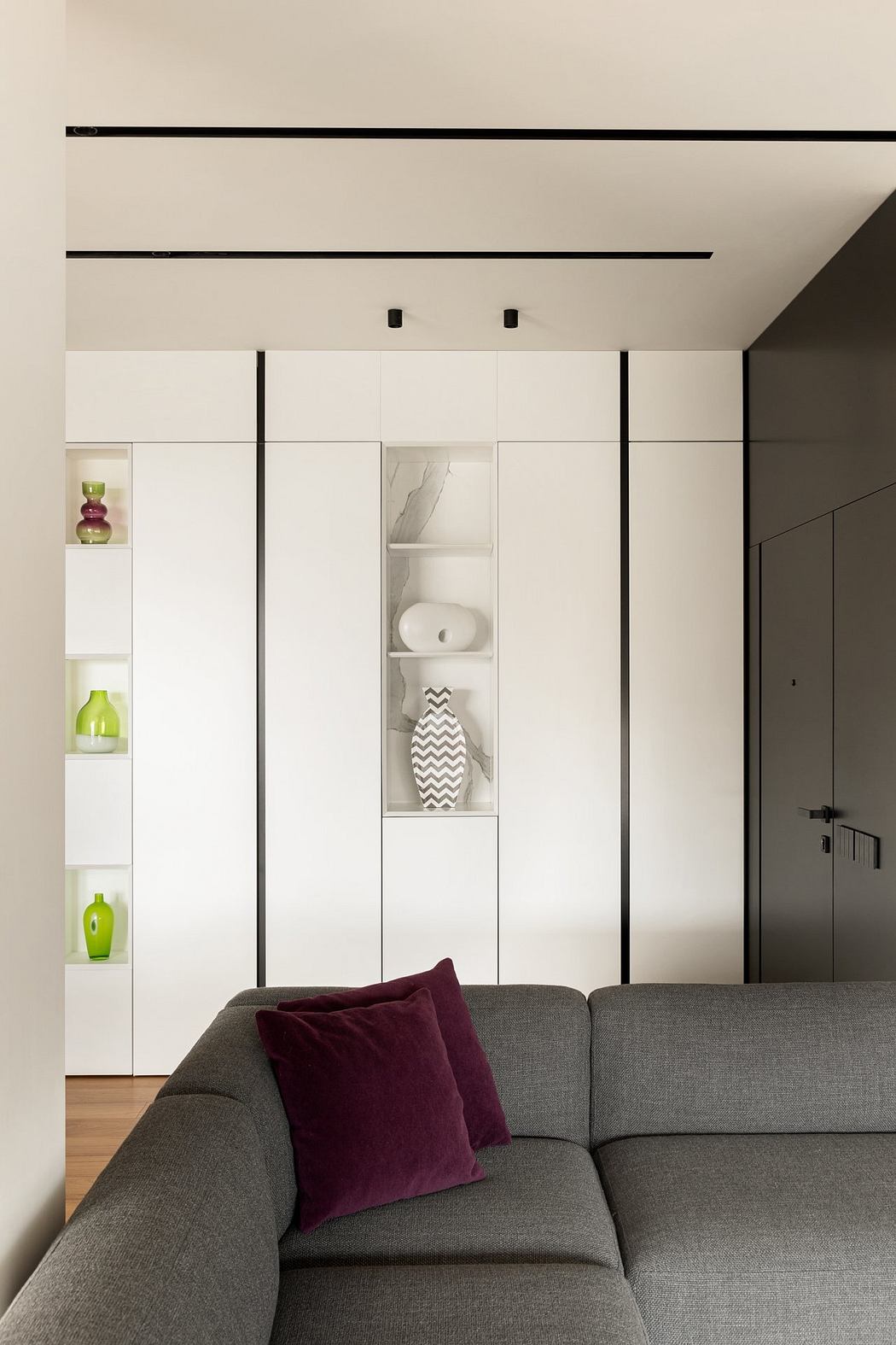 Minimalist living room with built-in white cabinets, gray sofa, and pops of green and purple.