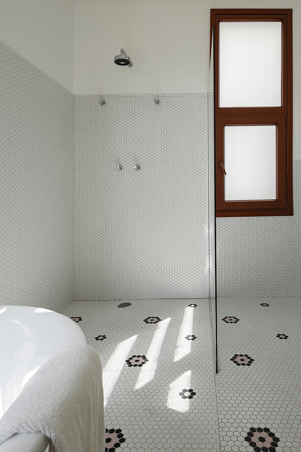 A modern bathroom with a white hexagonal tile floor and a wooden-framed window.