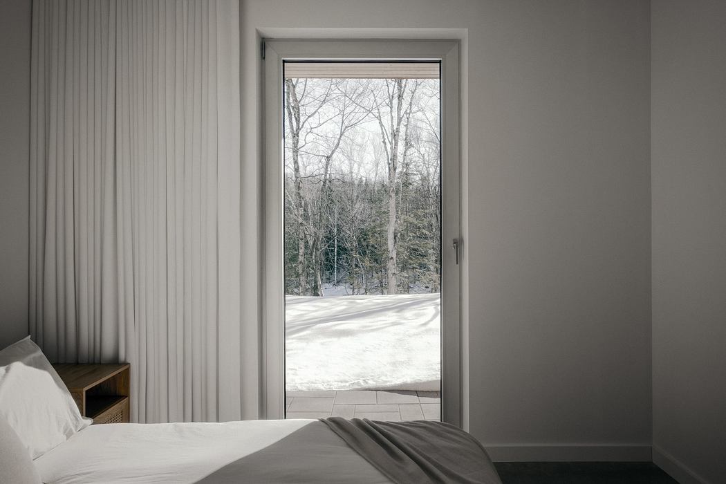 A cozy bedroom with a large window overlooking a snowy forest landscape.