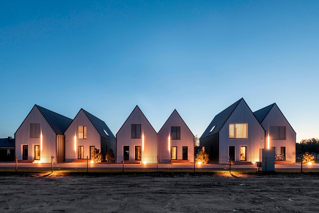 A row of stylish, contemporary houses with distinctive peaked roofs and warm exterior lighting.
