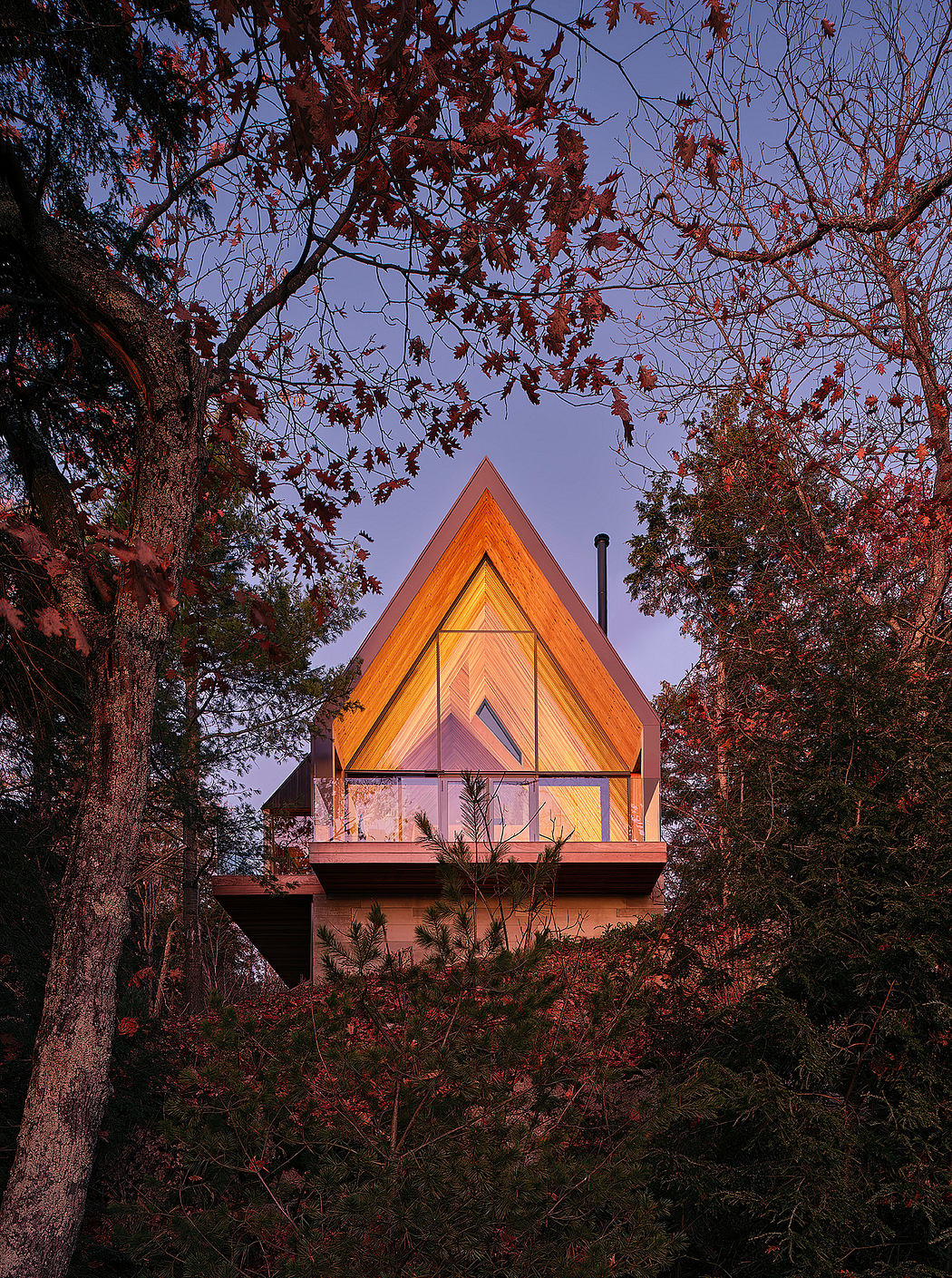 A cozy modern cabin nestled among autumn foliage, its sleek triangular design lit from within.