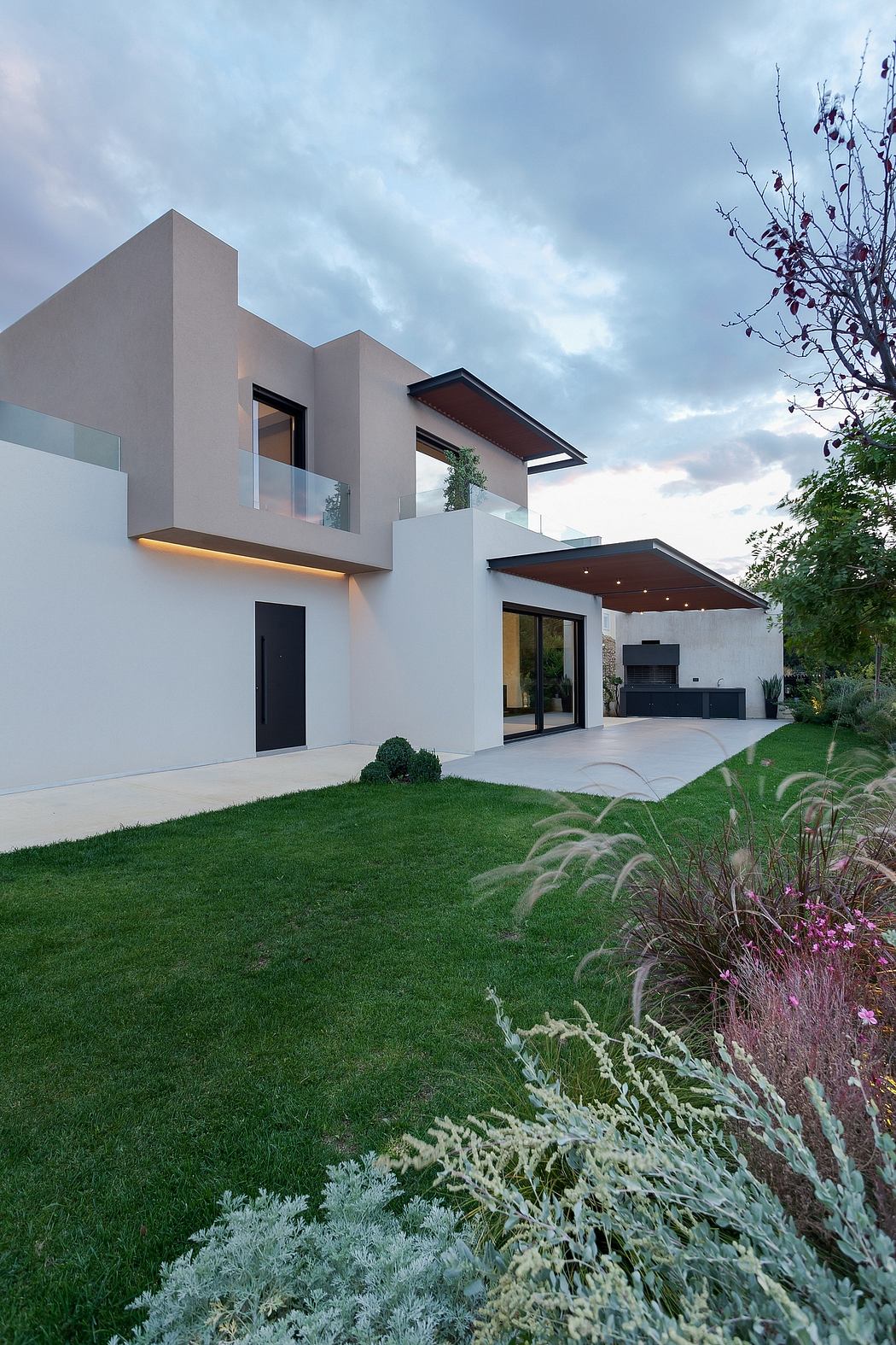 Modern, minimalist house with clean lines, large windows, and lush, landscaped yard.