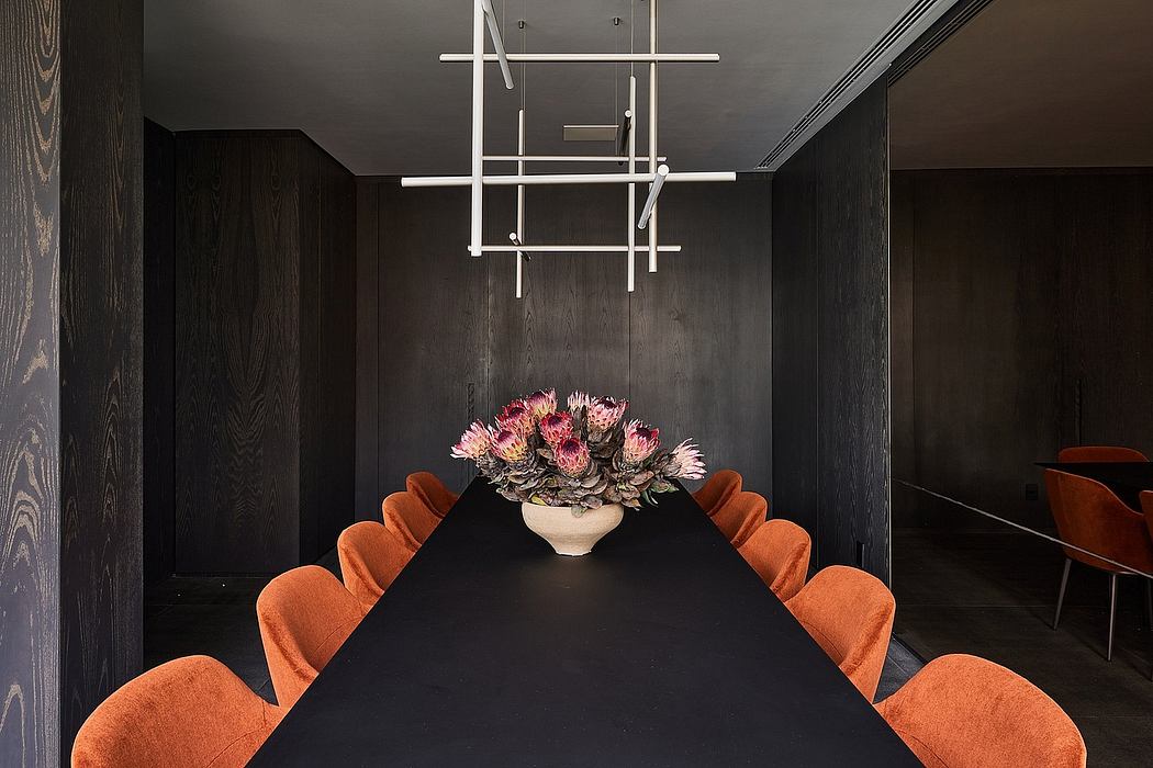 Sleek, modern dining room with dark wood paneling, geometric light fixture, and bold orange chairs.