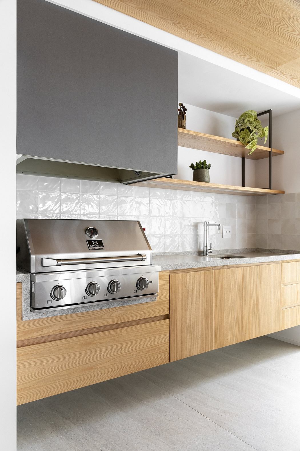 Modern outdoor kitchen with stainless steel grill, wooden cabinets, and minimalist shelves.