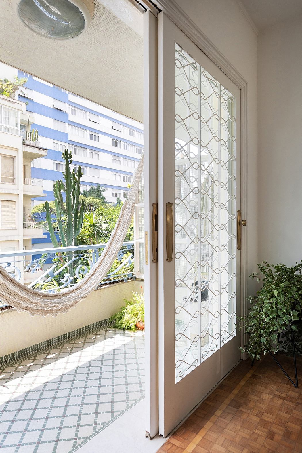 Cozy balcony with hammock, patterned sliding door, and lush plants overlooking urban view.
