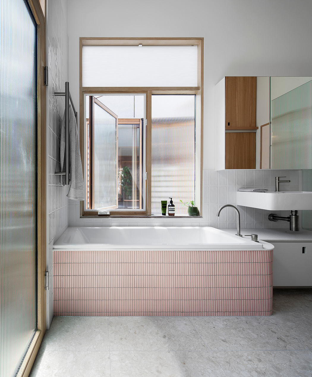 A modern bathroom with a minimalist design, featuring a large window, a pink-tiled tub, and wood accents.