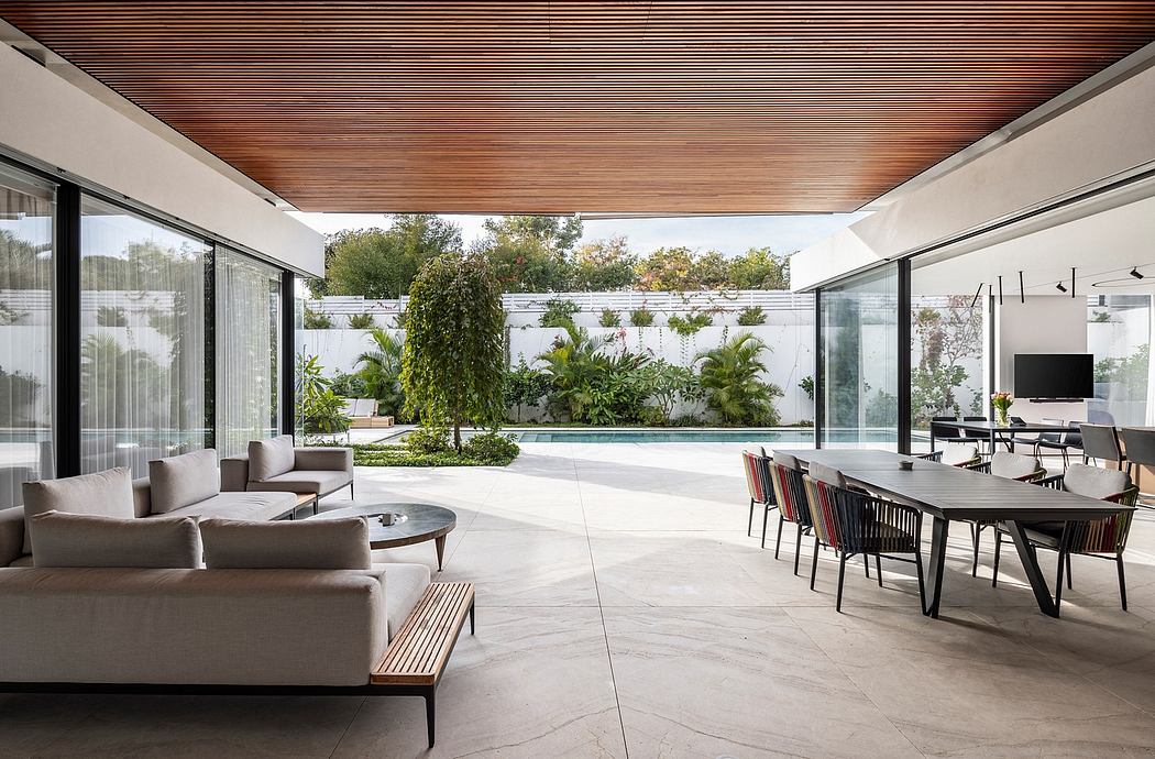 Expansive indoor-outdoor space with modern wood-paneled ceiling, lush greenery, and sleek furniture.
