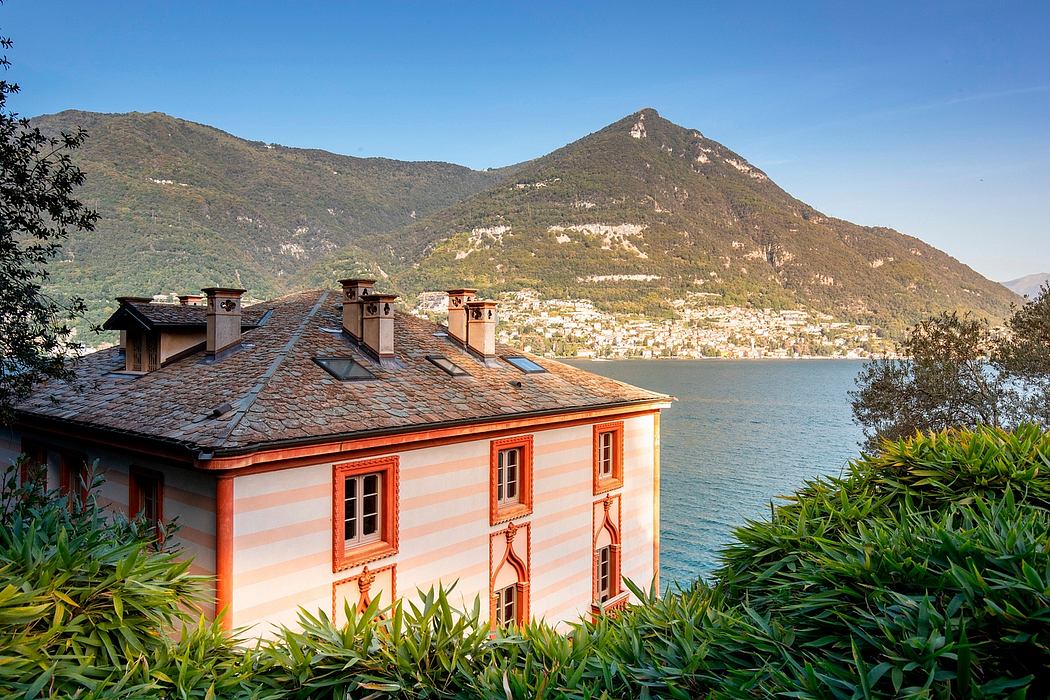 A charming lakeside villa with colorful facades, ornate windows, and lush greenery.