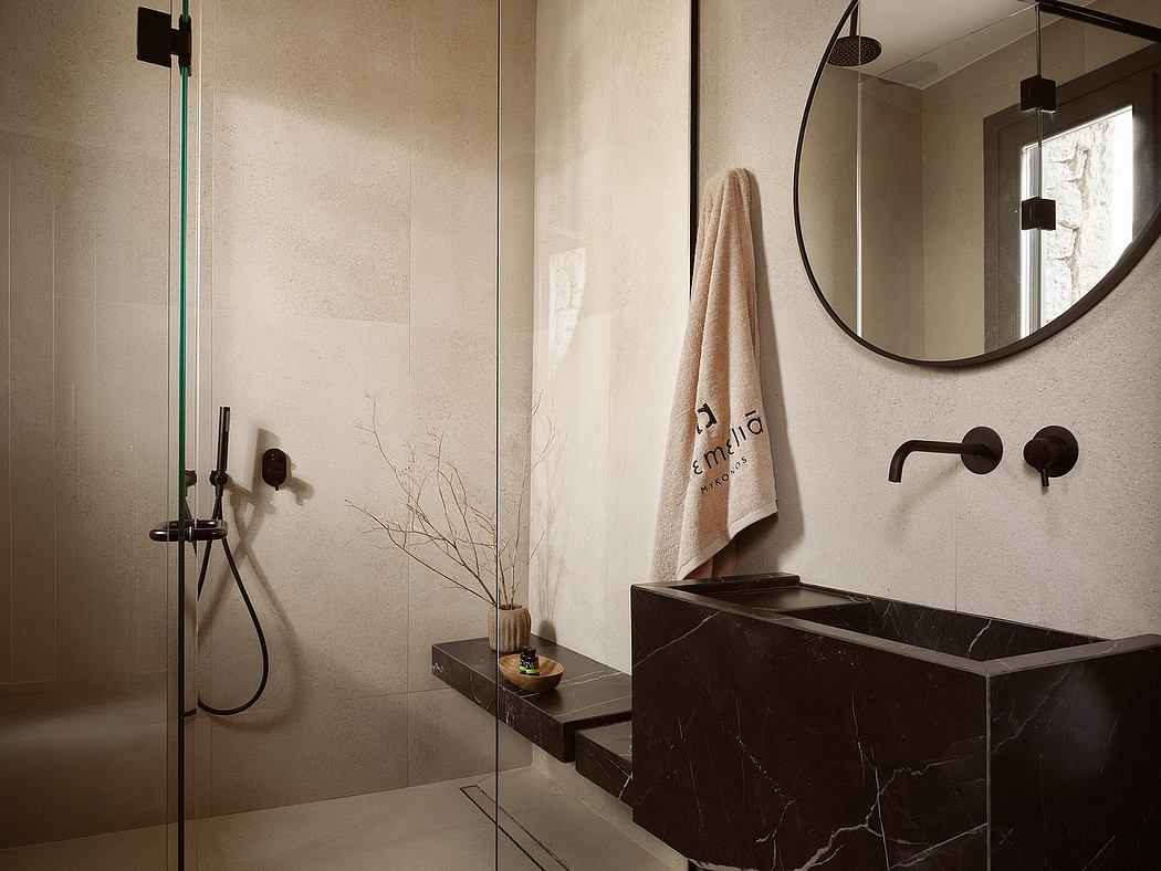 A modern, minimalist bathroom with a glass shower, a circular mirror, and dark marble sink.
