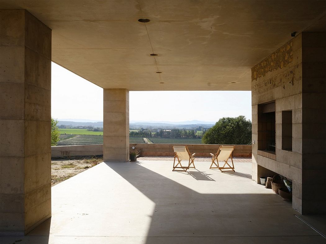 A covered concrete patio with wooden chairs overlooking a scenic countryside landscape.