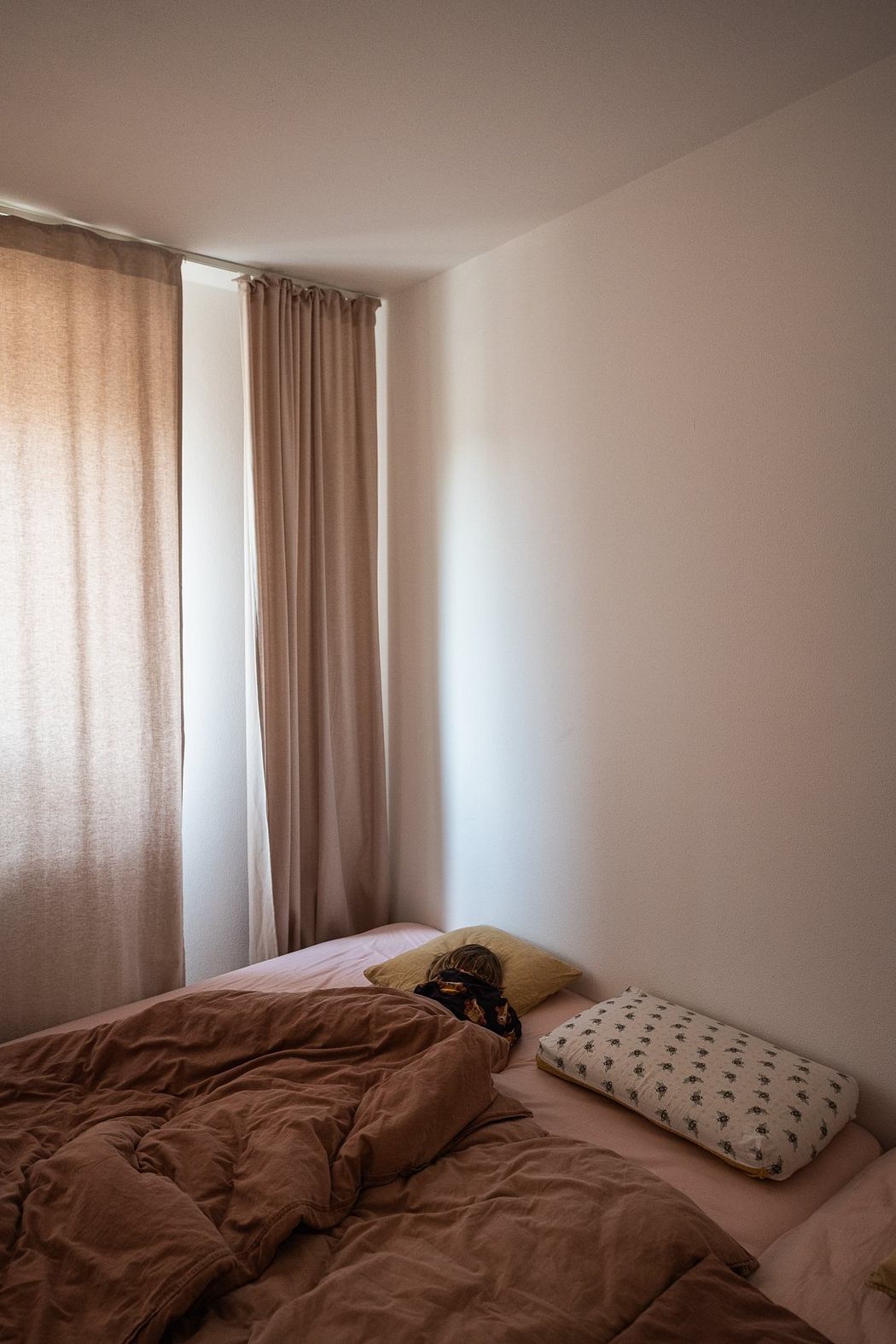 Simple, cozy bedroom with earthy tones, curtains, and soft bedding on a neatly made bed.