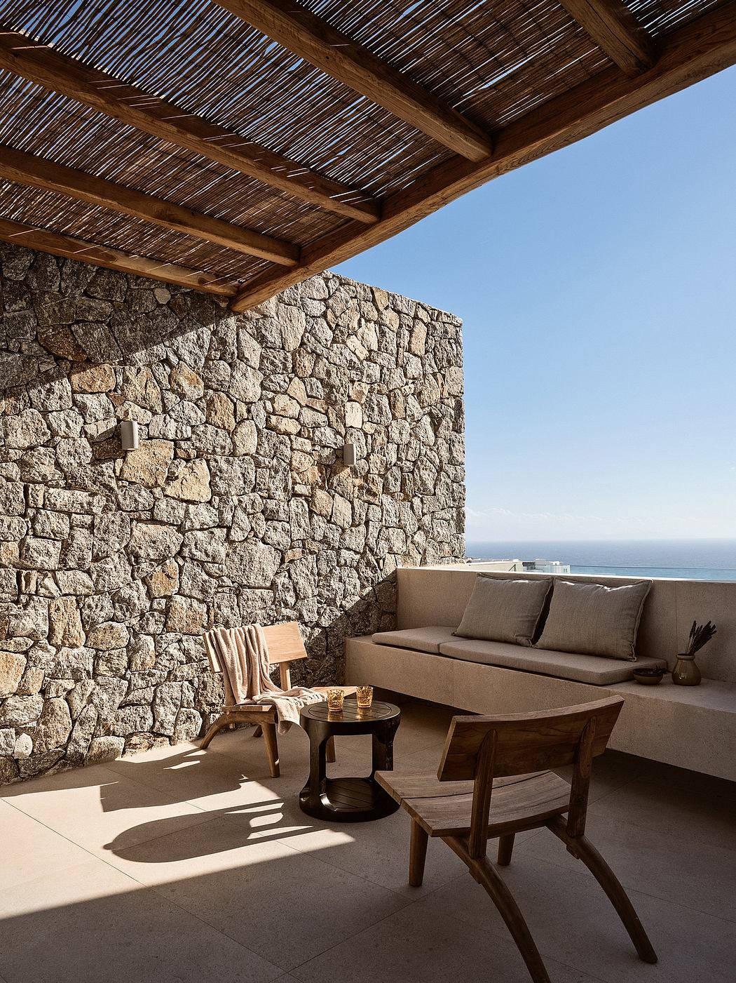 Rustic outdoor terrace with stone walls, thatched roof, and cozy seating area overlooking the sea.