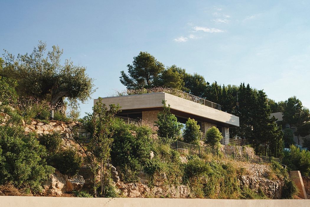 A modern, single-story building perched atop a rocky hillside, surrounded by lush greenery.