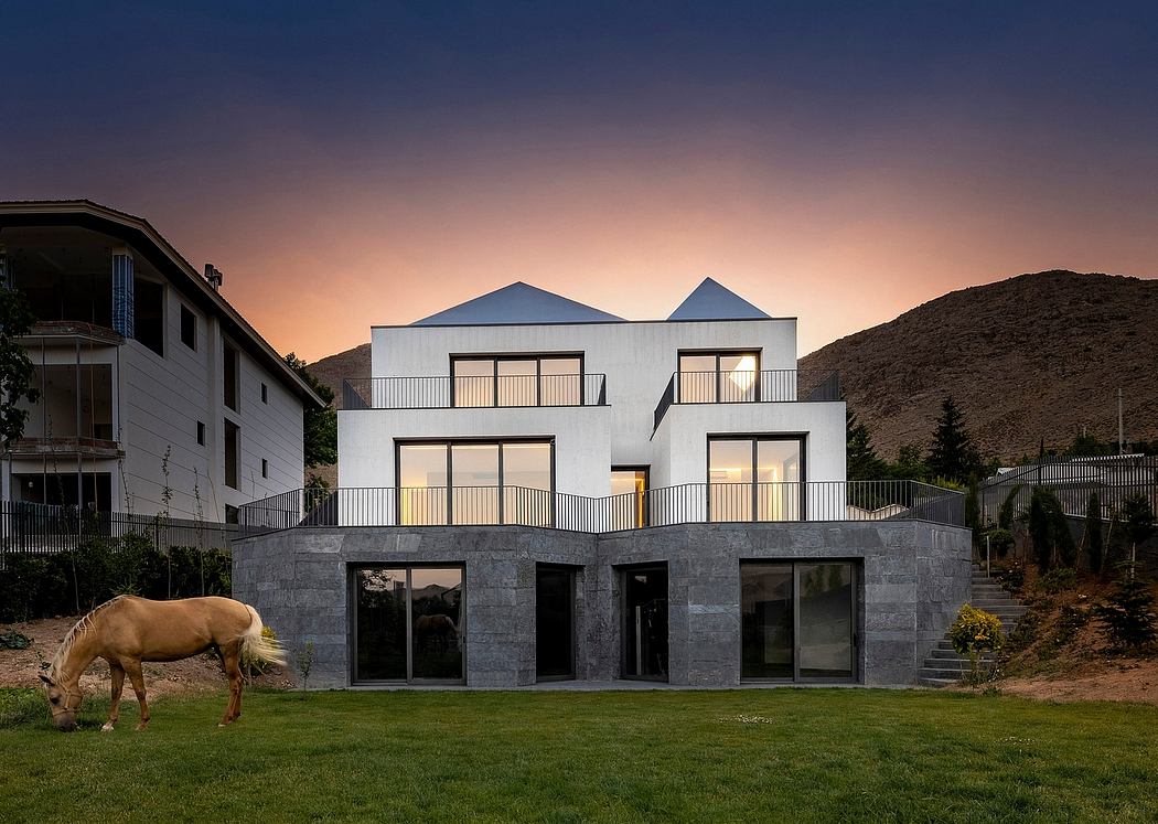 Modern white residential building with gabled roof and large glass windows overlooking a grassy lawn and mountain view.