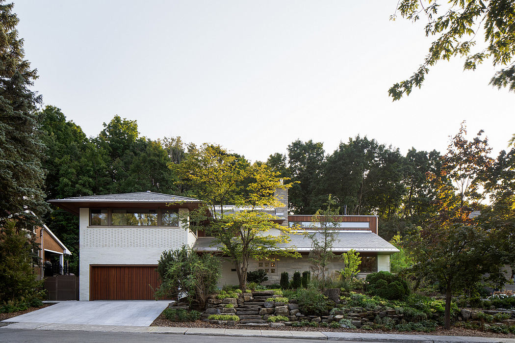 A modern, multilevel home nestled in a lush, wooded landscape, featuring a garage and landscaped exterior.
