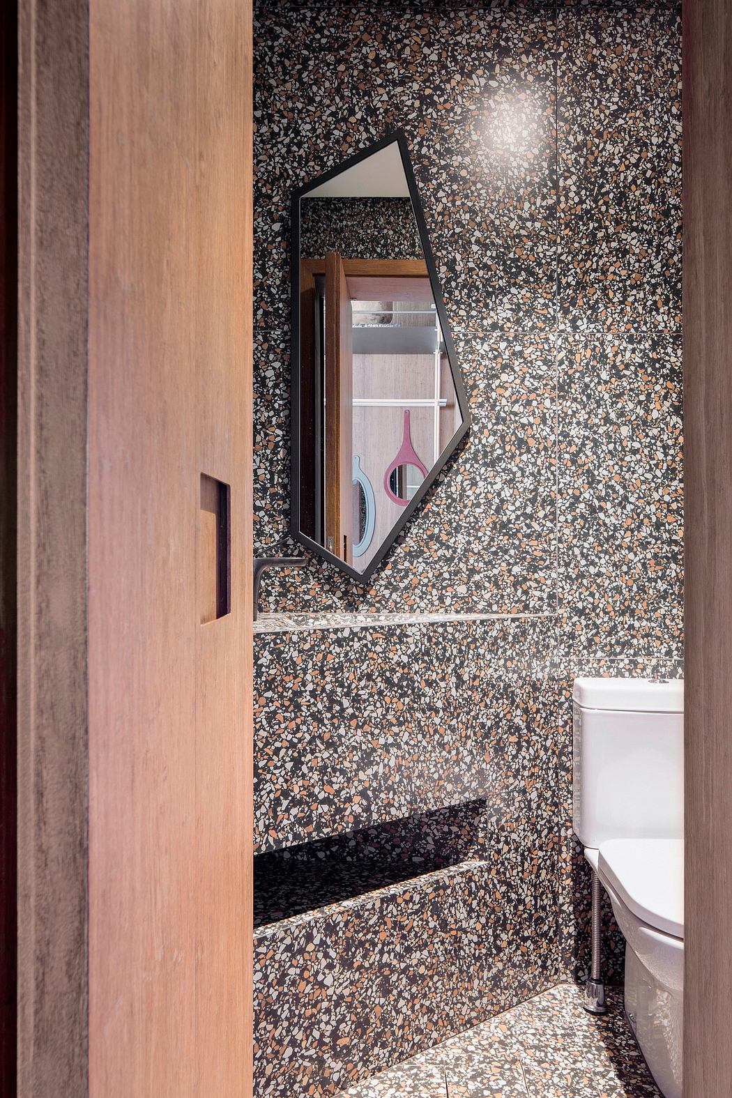 Eclectic bathroom design featuring a modern mirror and textured terrazzo walls.