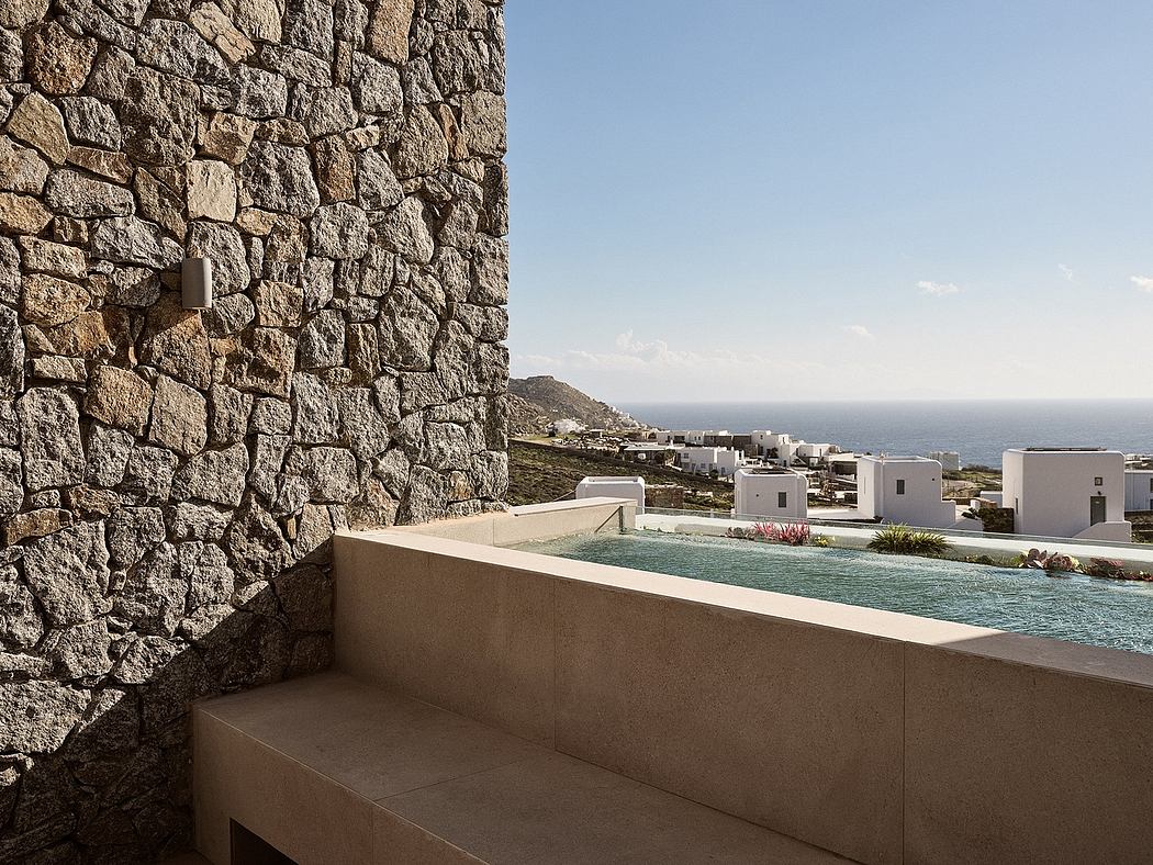 Minimalist architecture with a stone wall, pool, and scenic ocean view in the distance.