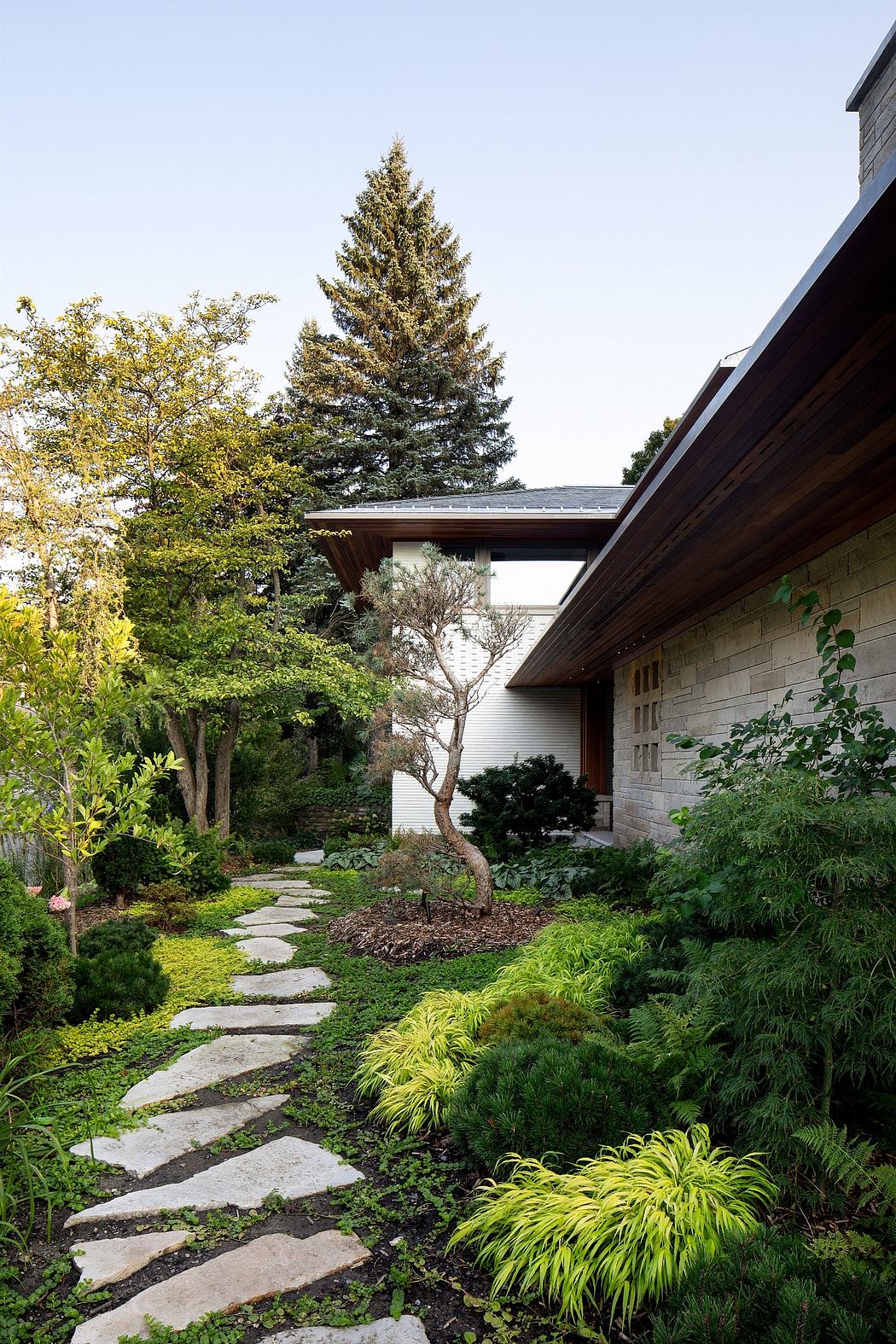 A serene, wooded landscape surrounds this modern, stone-clad residence with lush greenery.