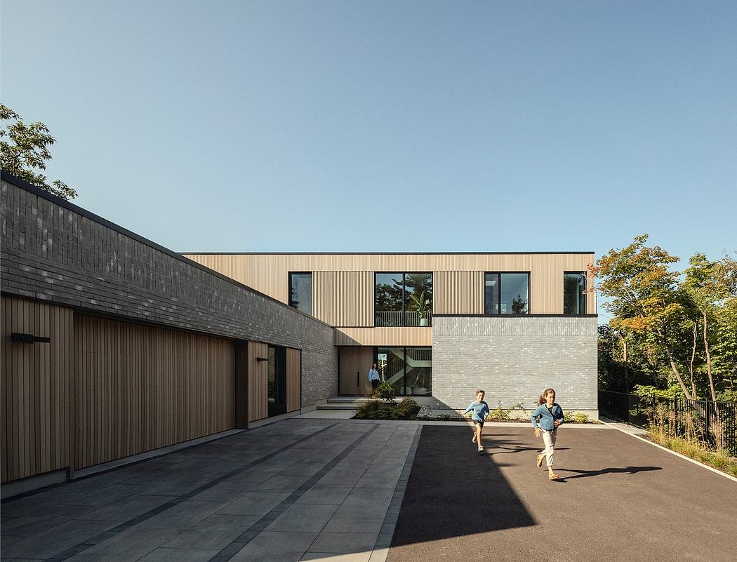 A modern, minimalist building with a combination of black and light wood siding, large windows, and a long driveway.