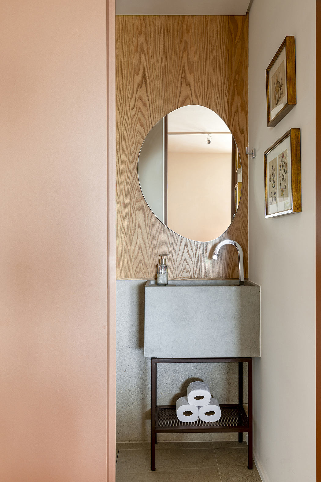 Bathroom with wooden paneling, round mirror, concrete vanity, and storage shelf.
