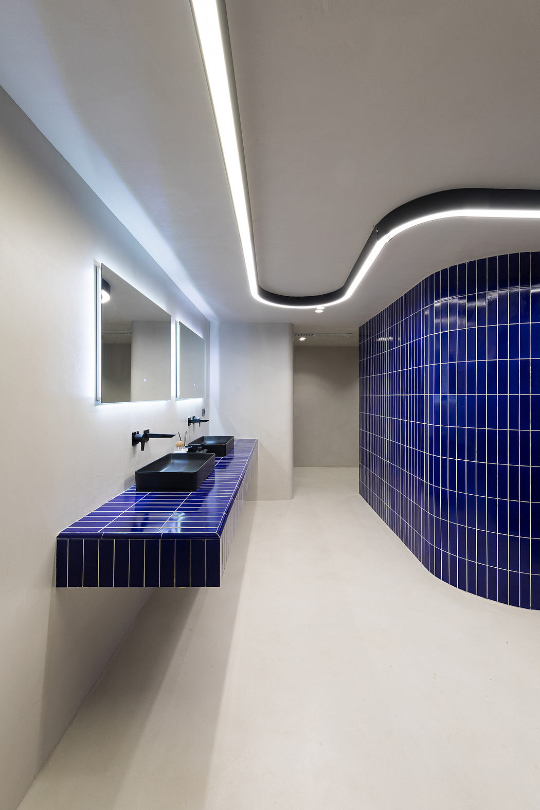 A modern bathroom with minimalist design, featuring a blue tiled wall and floating vanity.