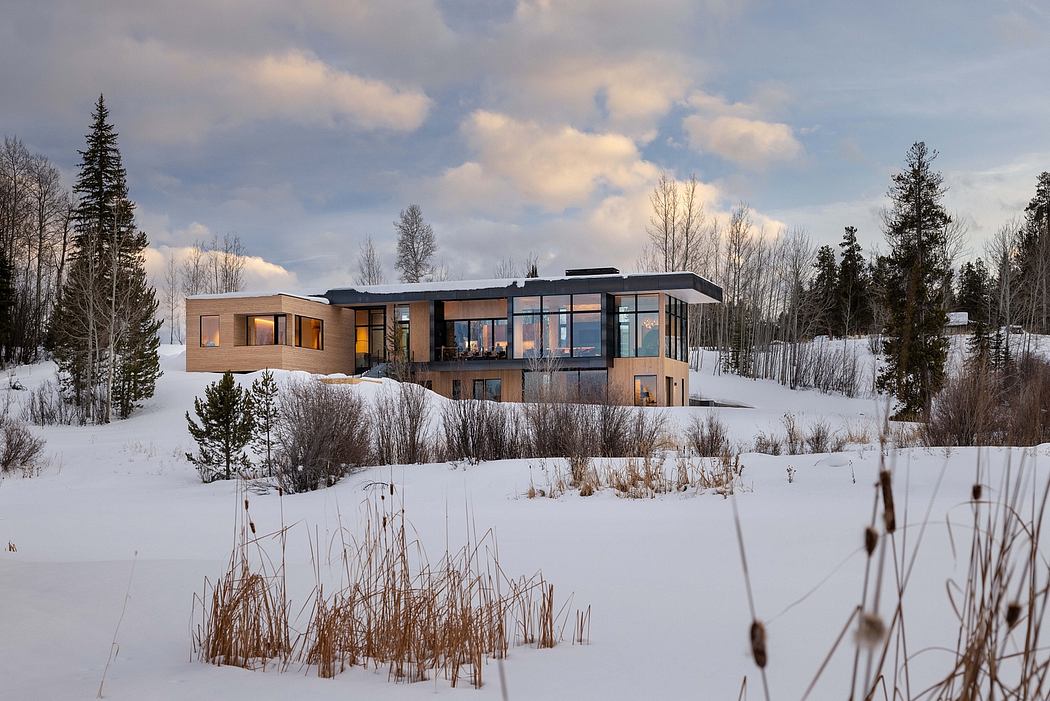 A modern, multi-story house with glass walls and a sleek, contemporary design nestled in a snowy landscape.