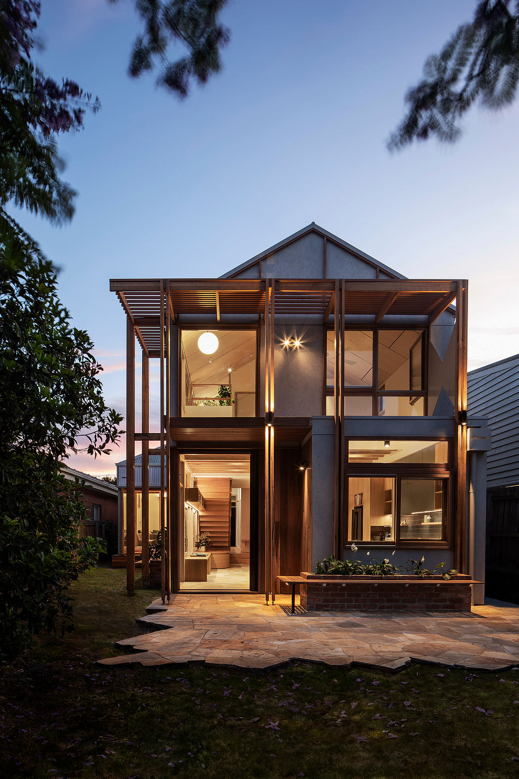 A modern, wooden home with a striking roofline, large windows, and a paved outdoor area.