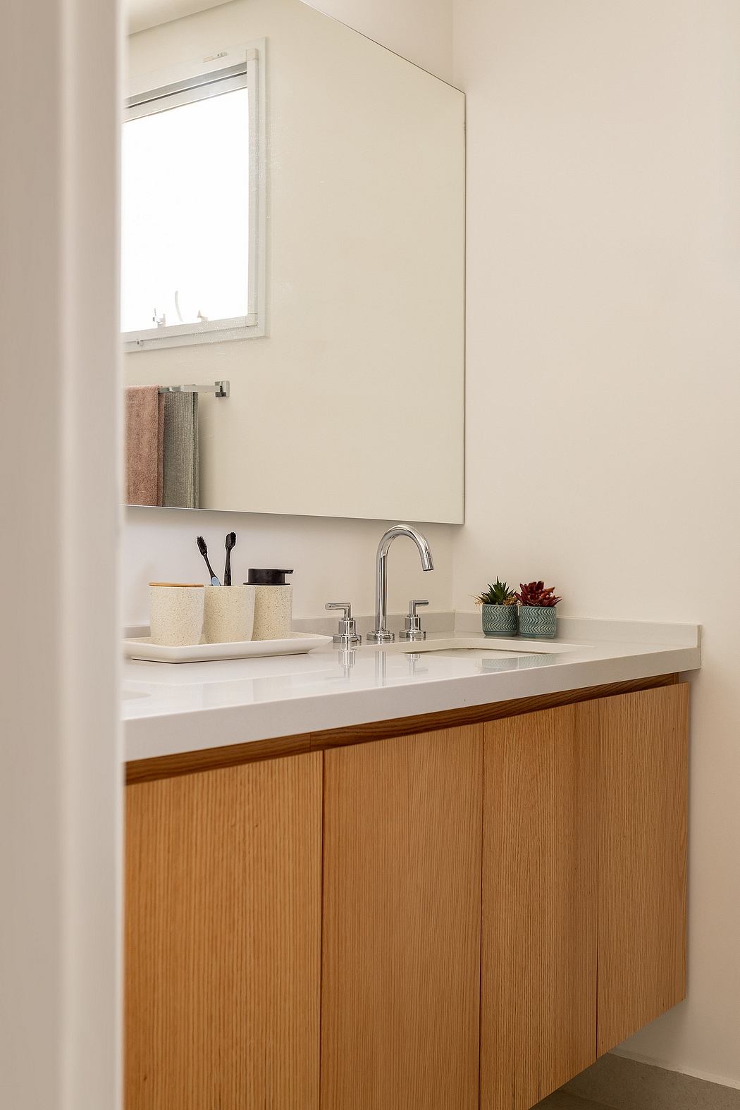 Modern bathroom vanity with white countertop, wood cabinets, and sleek chrome fixtures.