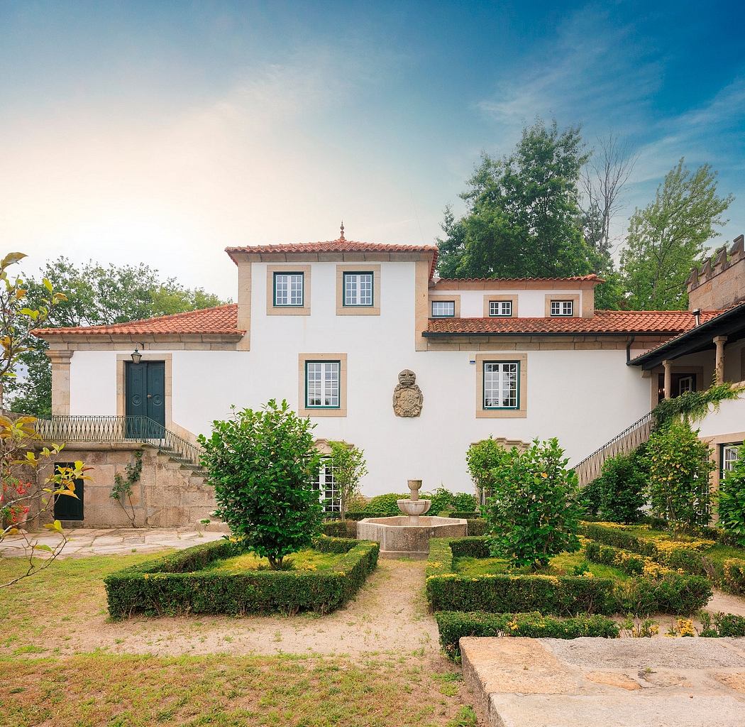 Charming Portuguese manor with red-tiled roofs, arched windows, and lush garden.