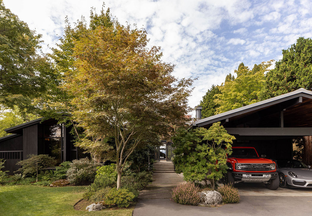 Autumn-tinted foliage frames a modern lodge with a red Bronco parked in the driveway.
