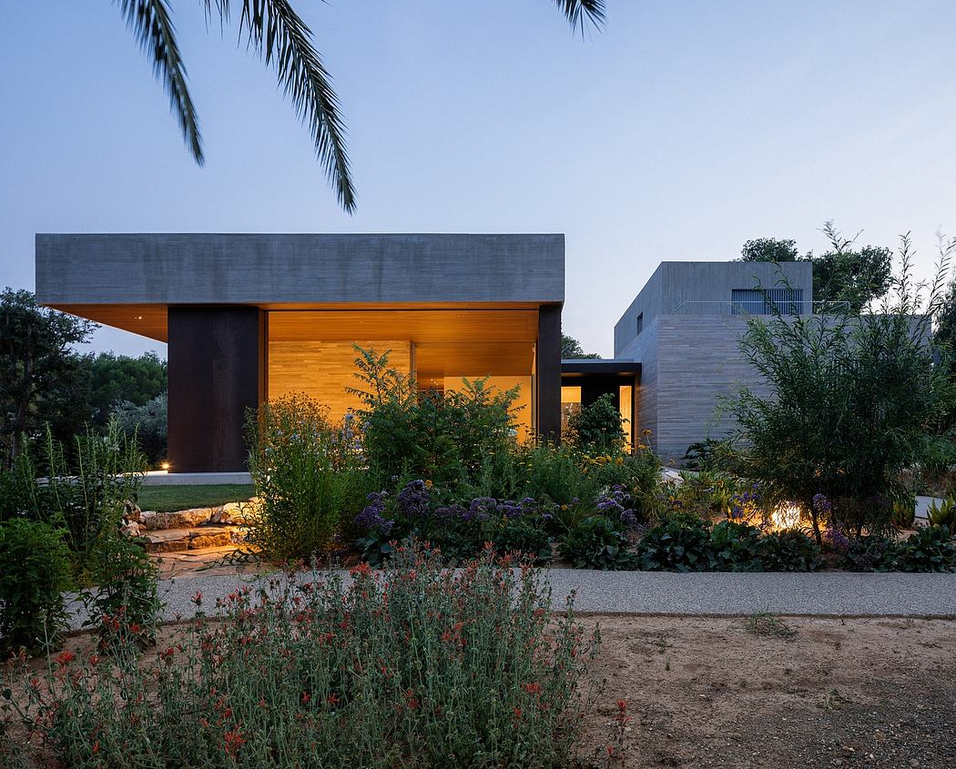 A modern concrete and wood structure with lush landscaping and exterior lighting.
