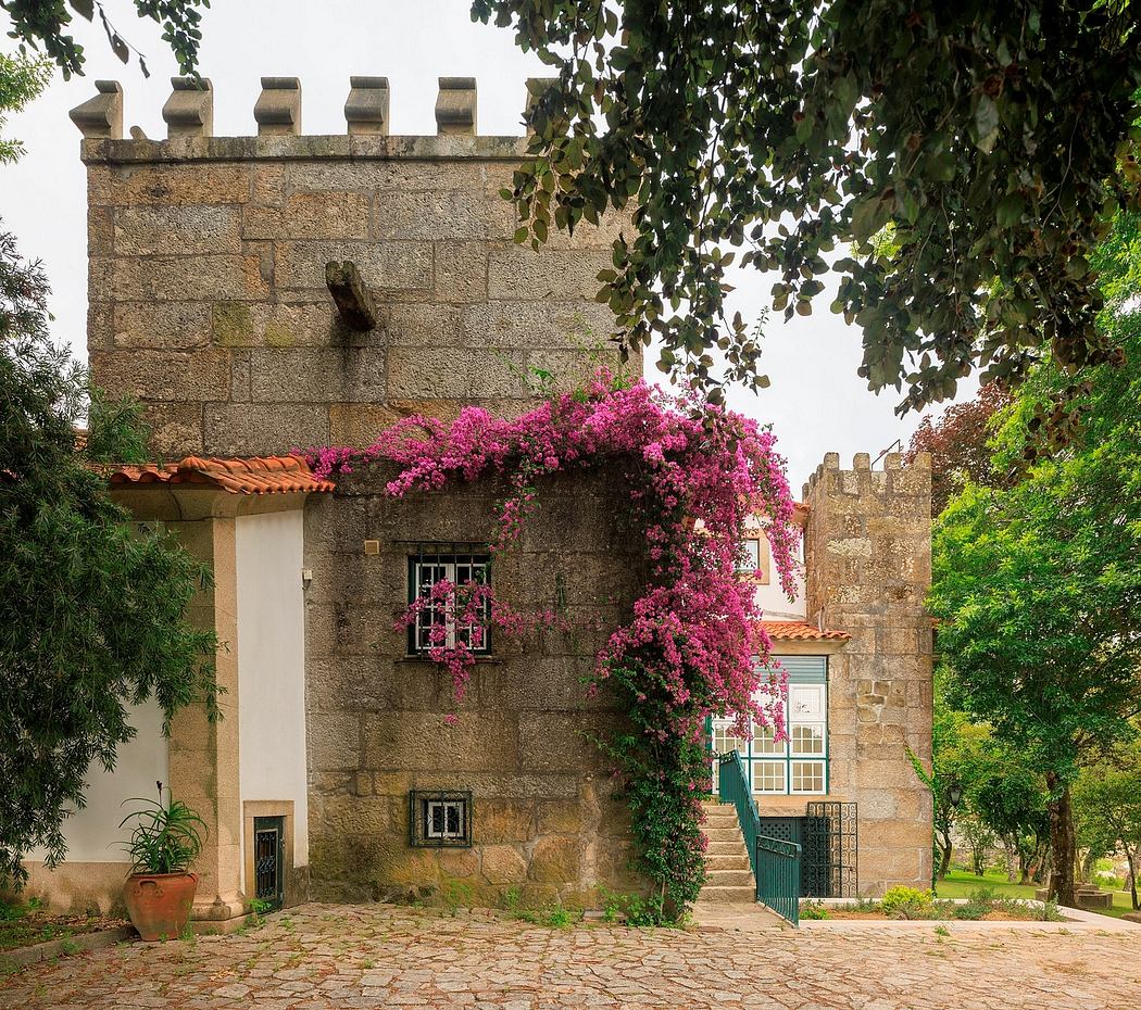 A charming stone castle-like structure with a vibrant bougainvillea-covered pergola, nestled in lush greenery.