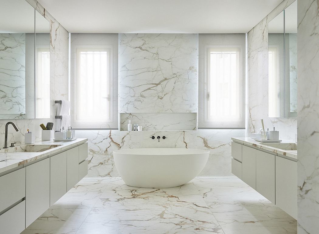 Spacious marble-clad bathroom with freestanding tub, clean-lined vanities, and large windows.