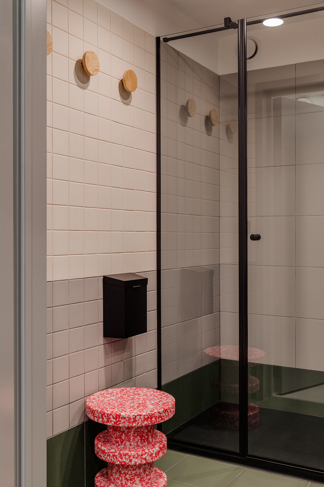 A contemporary bathroom design featuring a glass shower enclosure, tiled walls, and a red patterned stool.