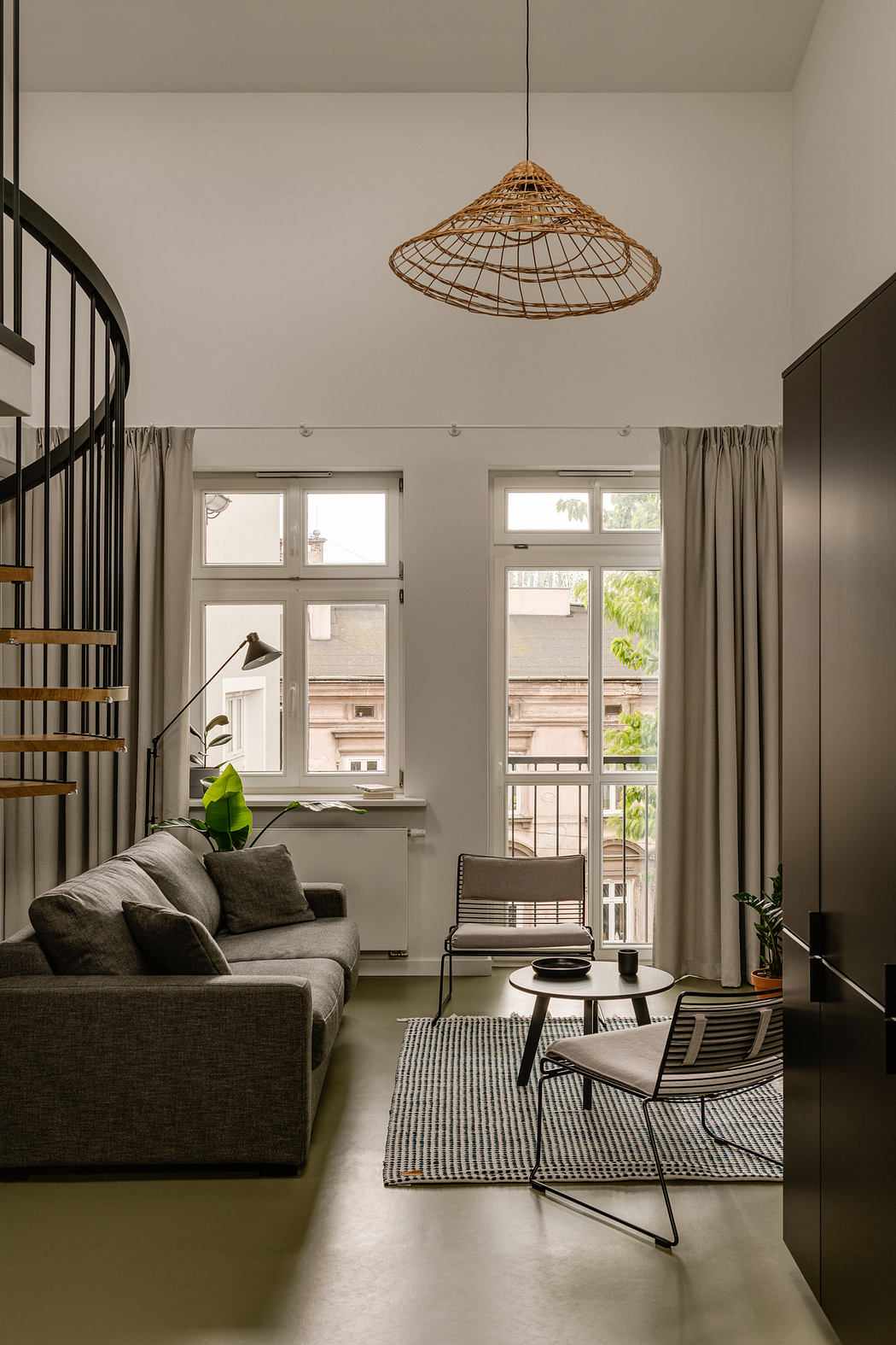 A cozy living room with a woven light fixture, minimalist furniture, and floor-to-ceiling windows offering a view of the outdoors.