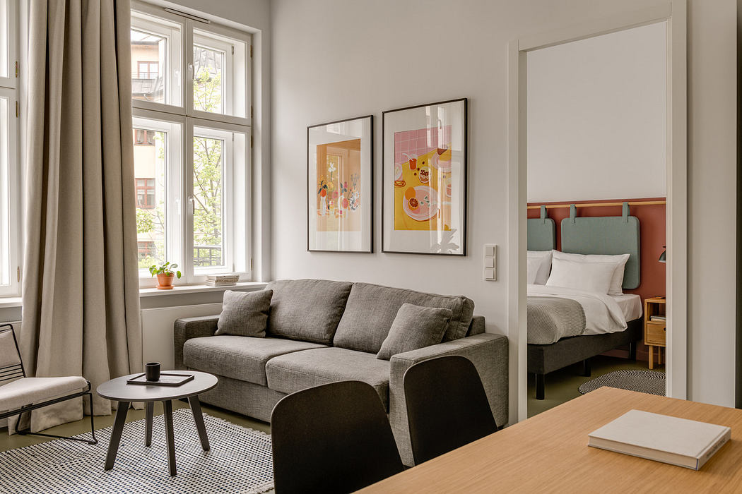 Cozy modern living space with large windows, gray sofa, and framed artwork on walls.