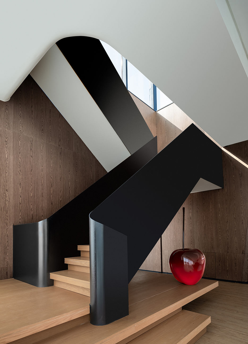 Modern architectural staircase with contrasting black and wood tones, accented by a large red apple sculpture.