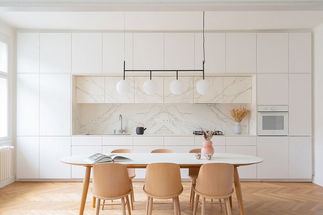 Minimalist kitchen interior with sleek white cabinetry, marble backsplash, and wooden furnishings.