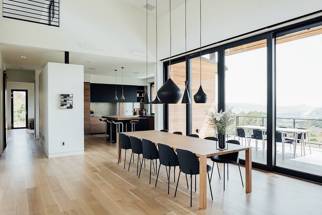 Sleek, modern kitchen and dining space with wooden floors, black furnishings, and floor-to-ceiling windows.