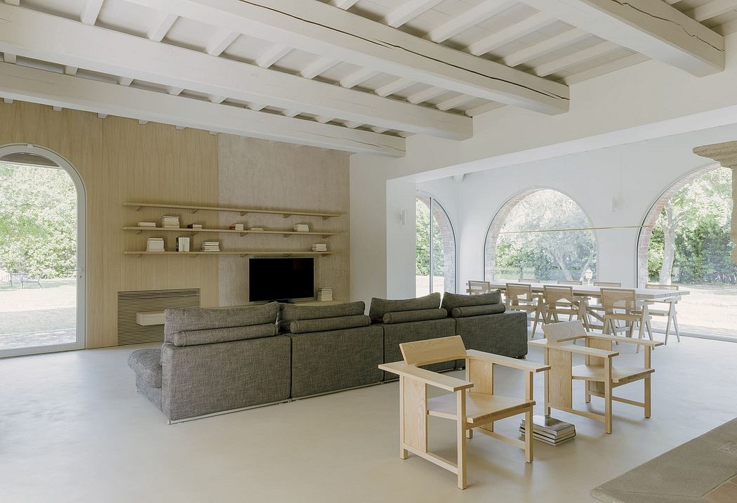 Modern, minimalist living space with wooden beams, shelving, and arched windows overlooking nature.