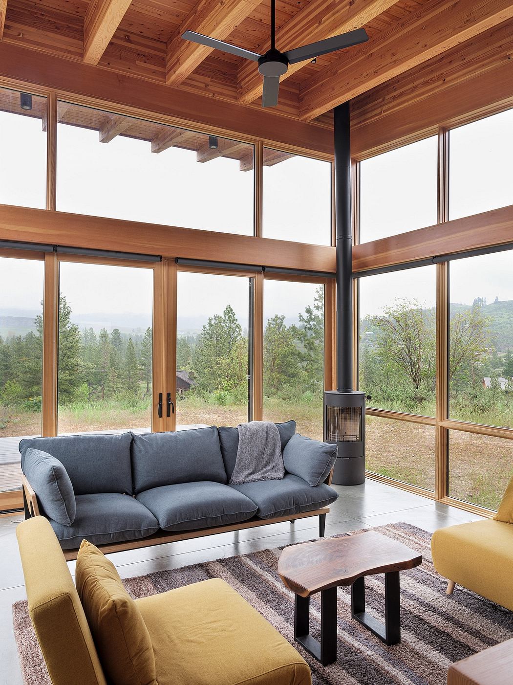 Cozy cabin interior with wood-paneled ceiling, large windows, and modern furniture.