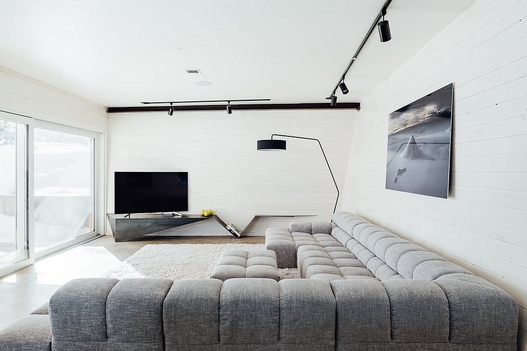 Minimalist living room with white walls, track lighting, large sectional sofa, and artwork.