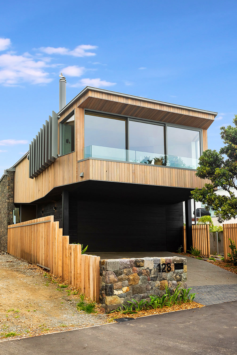 Modern two-story house with wooden siding, glass balcony, and stone foundation.