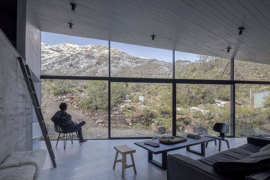 A contemporary, glass-walled interior with a stunning mountain view, featuring minimalist furniture and decor.