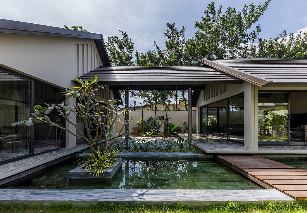 Modern, open-plan home with glass walls, shallow pool, and lush landscaping.
