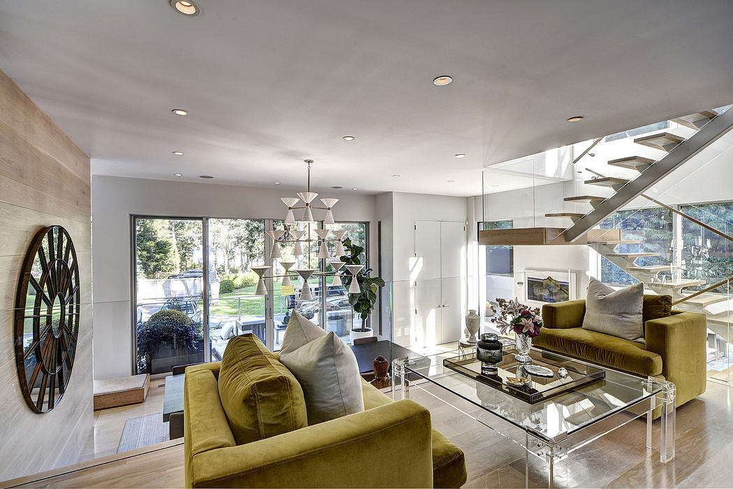 Luxurious living room with modern furniture, glass staircase, and views of lush greenery.