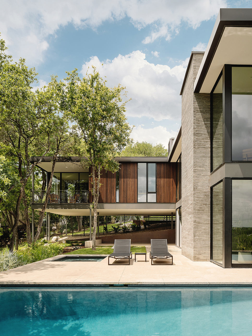 Modern, open-concept home with a pool overlooking lush greenery and a cloudy sky.