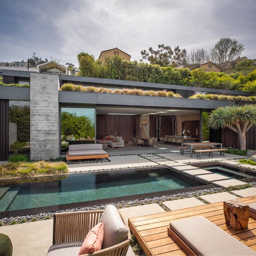 A modern, open-plan home with a sleek concrete structure, lush landscaping, and a stunning pool.