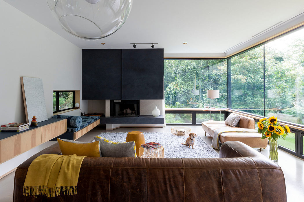 Large glass windows offer a serene forest view in this stylish living room with a modern fireplace.