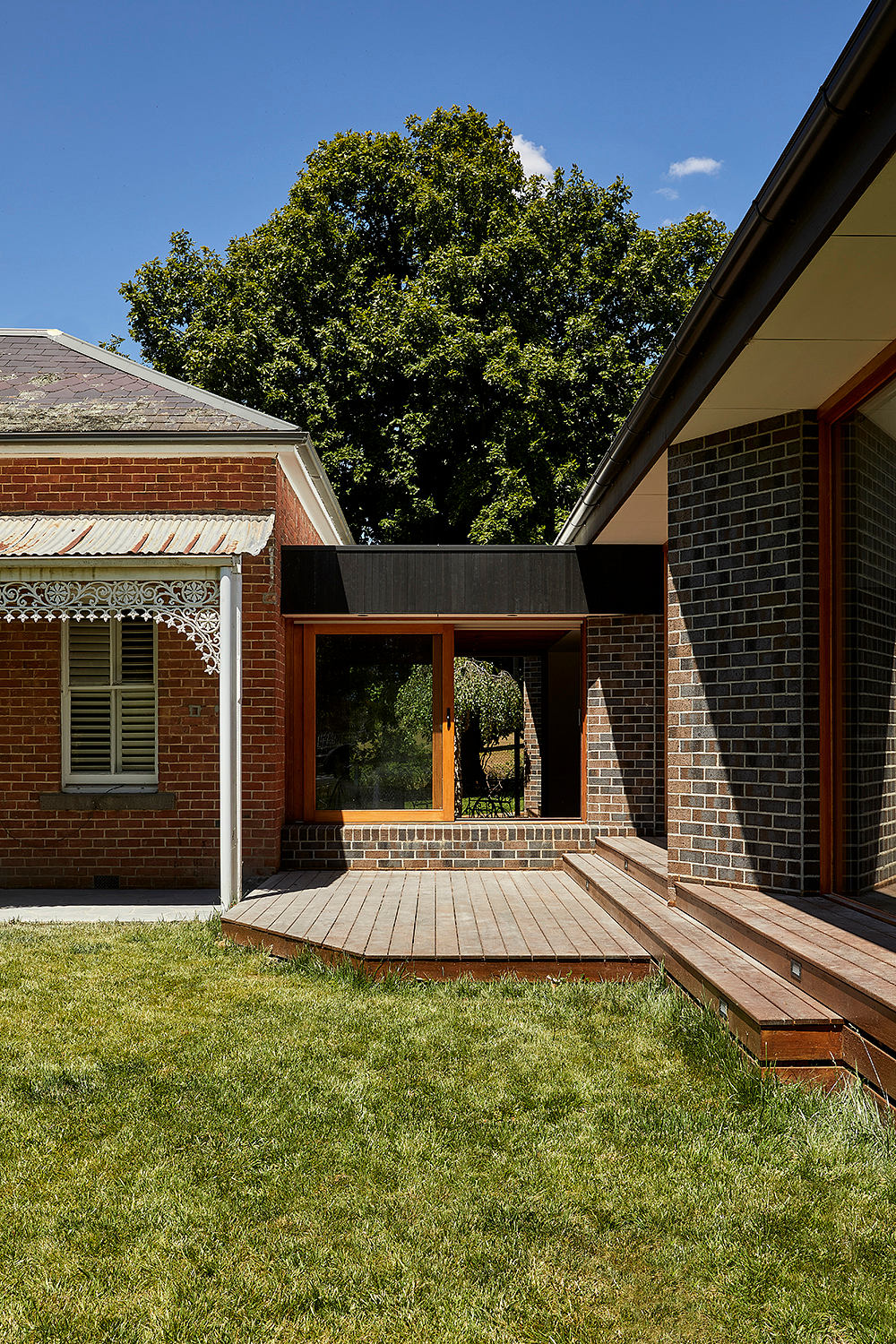 Elegant brick home with a modern wood-paneled entryway, surrounded by lush greenery.